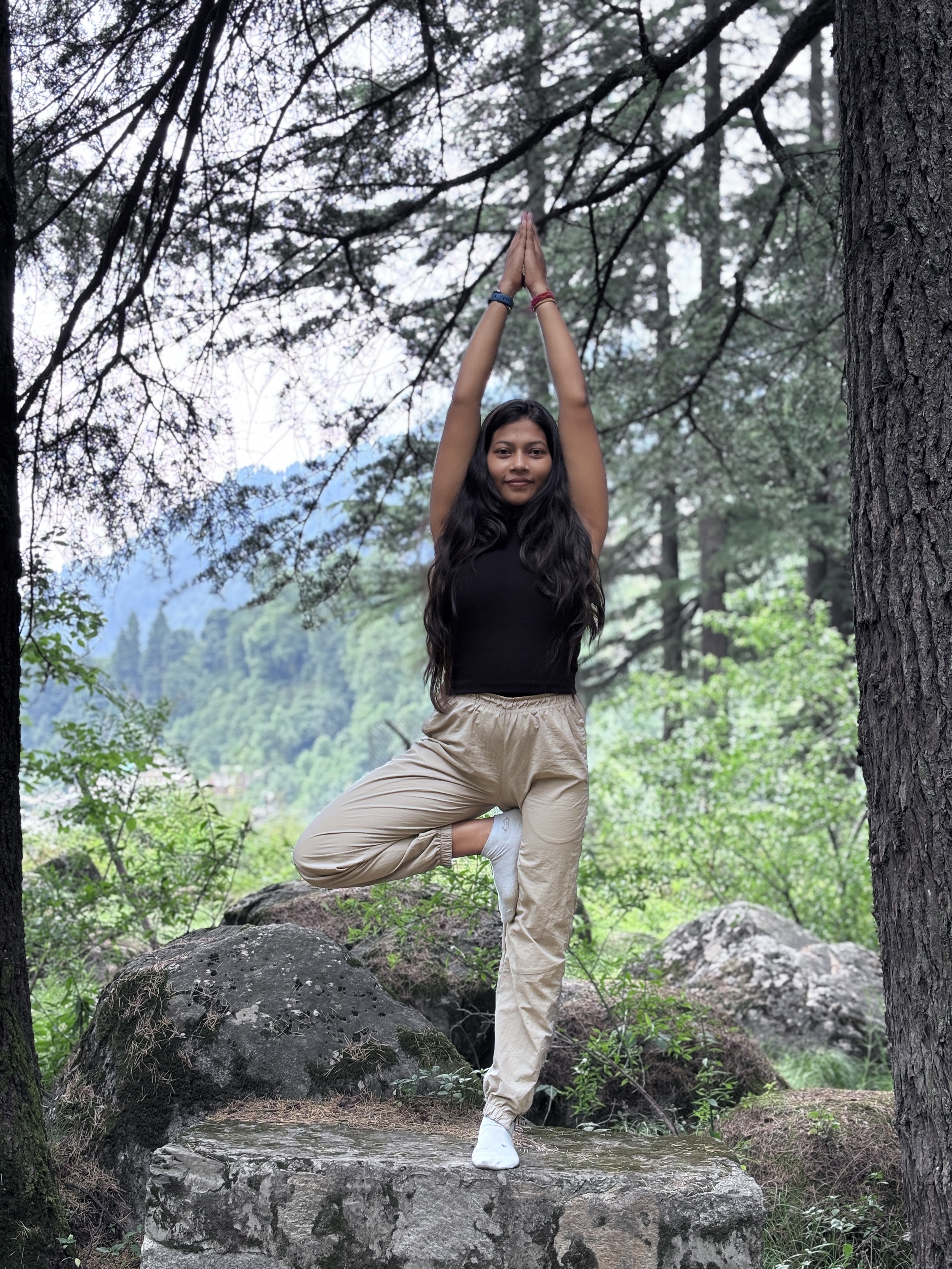 Purnima holding Tree Pose with hands in prayer overhead in a serene Himalayan forest